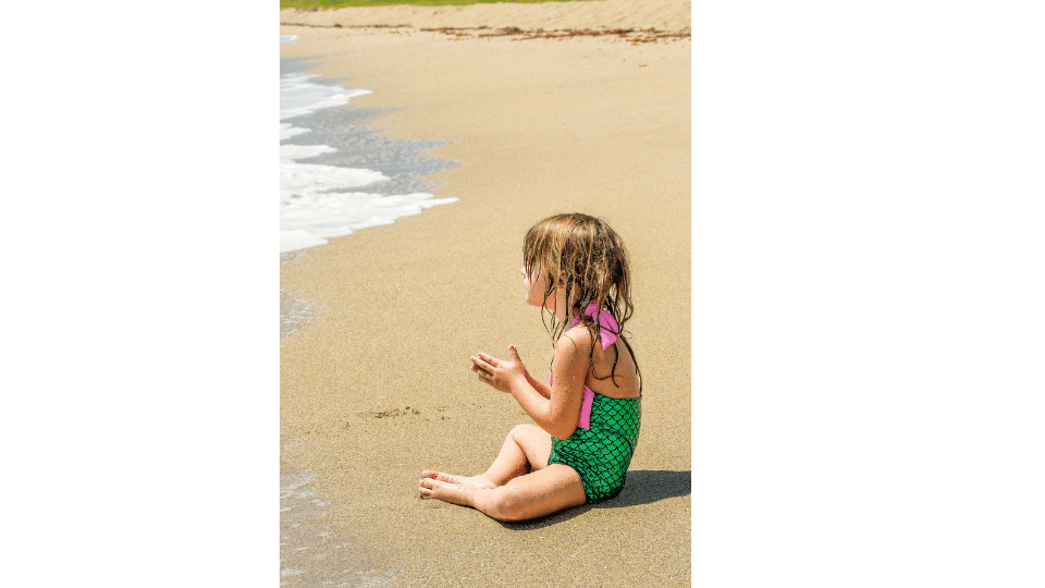 petite fille assise sur la plage en maillot sirene